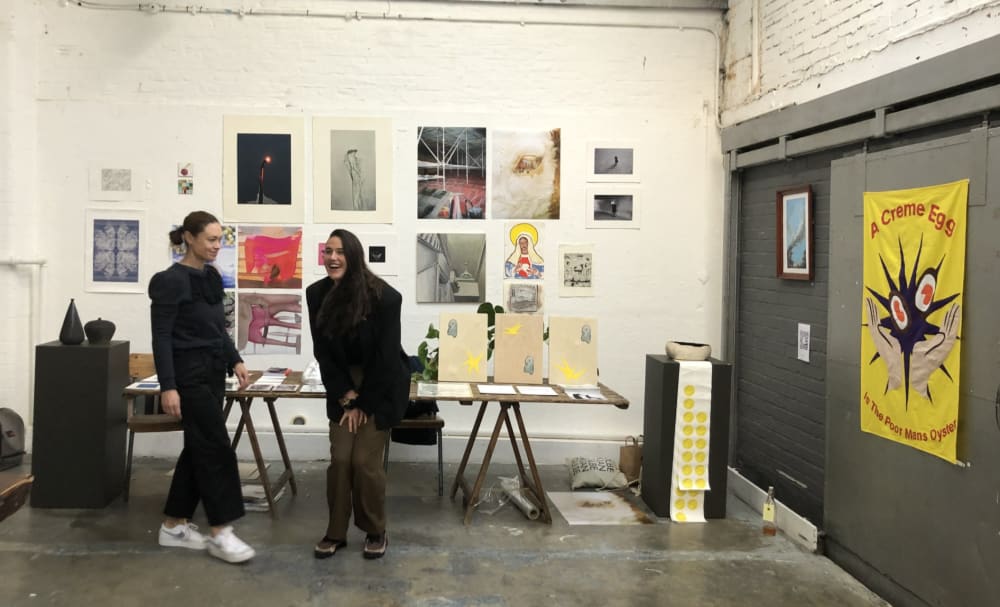 Two women in front of a gallery wall filled with artwork.
