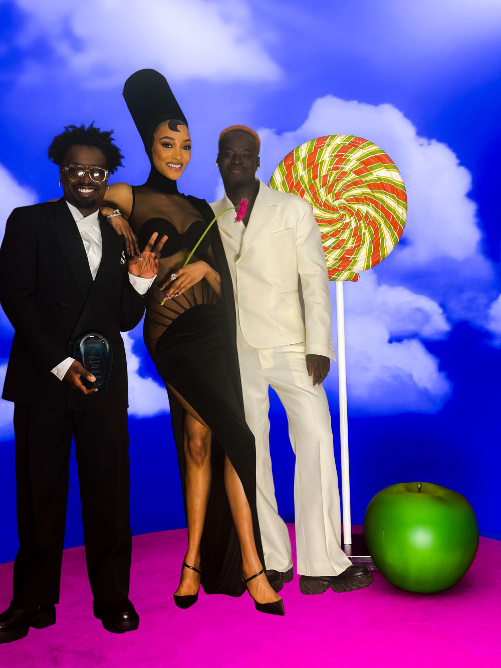 Campbell, Jordan and Ib standing in front of a bright blue background. There's a giant lollipop and giant apple to the right