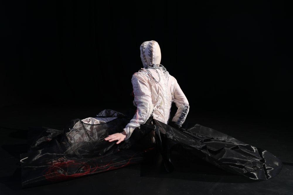 Model sat on stage wearing white draped costume