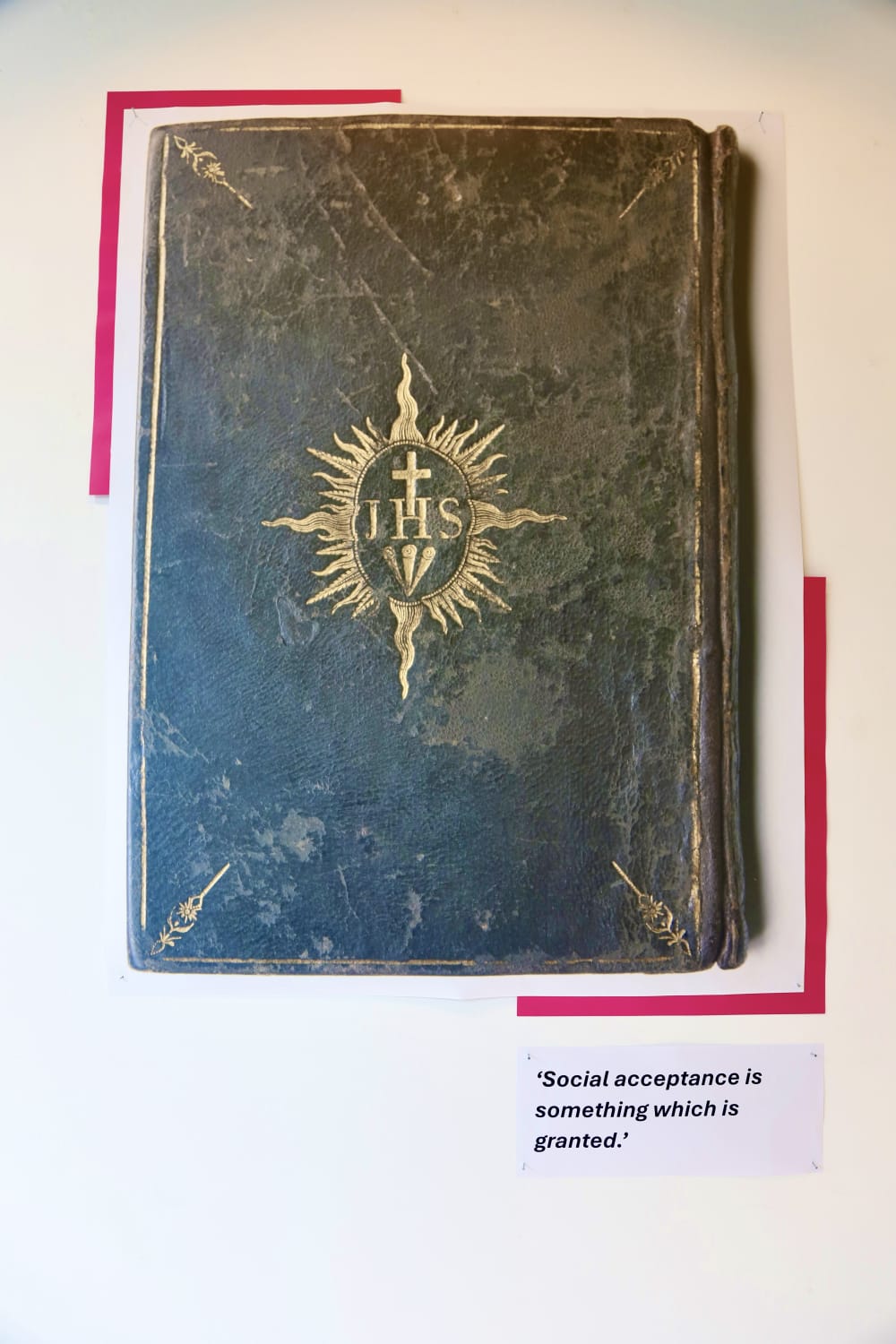 A blown up reproduction of the cover of the 18th prayer book that belonged to Mademoiselle la Chevalier d'Eon, against a white wall. A text panel reads 