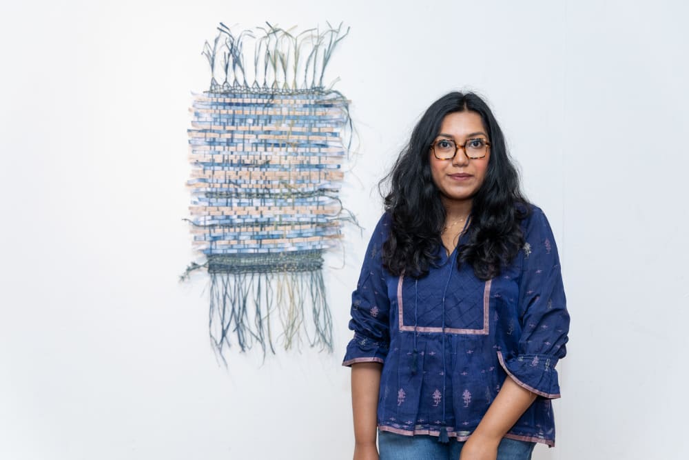 Anika standing next to her work, a woven piece in blue and white