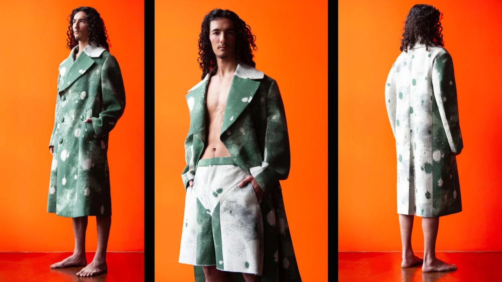 Model wearing bespoke tailored coat and trousers against vibrant orange backdrop.