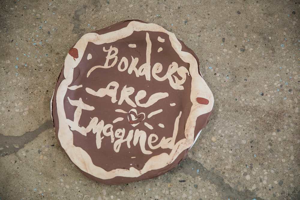Close up of a round clay slab with embossed handscript wording 'Borders Are Imagined' and a loveheart symbol.