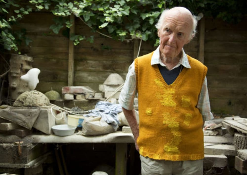 an elderly man in a garden, wearing a knitted yellow sweater