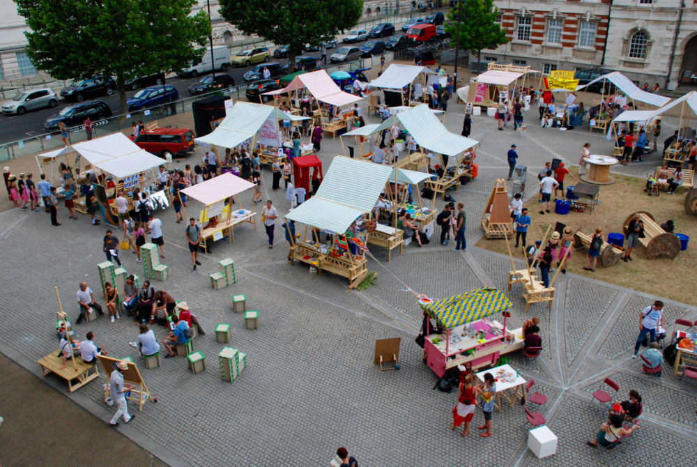 Aerial photograph of a large paved open space filled with people and wooden market stalls.