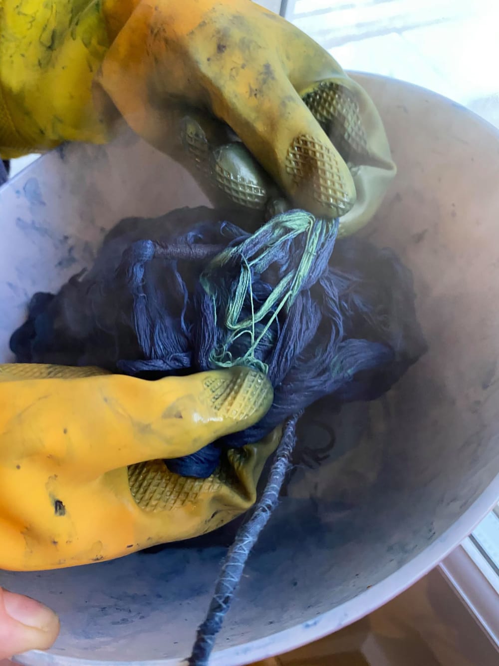 close up of hand dying material blue in bowl, with two hands in yellow rubber gloves