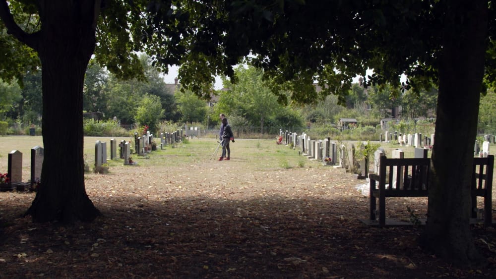 Photo of a graveyard taken from between two trees. Two men stand looking at a gravestone