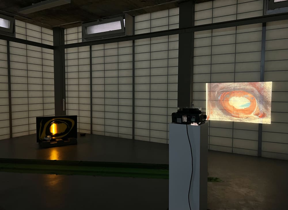 A shot of a dark room, there is a projector  displaying an artwork piece onto the wall