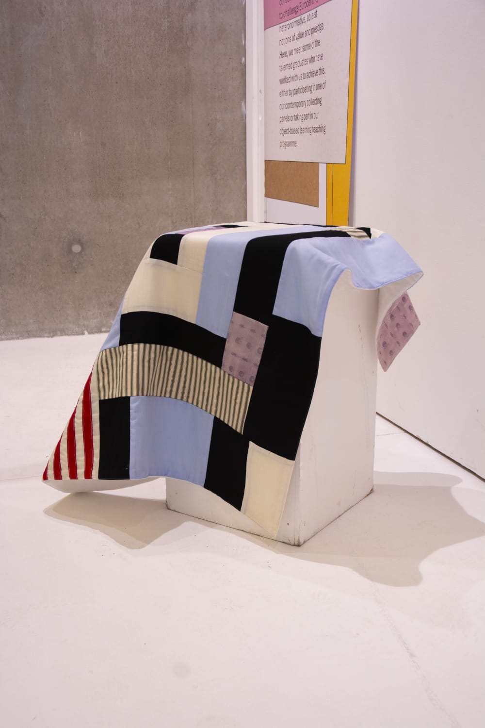 Patchwork quilt with blue, black, white, purple and striped grey squares laid on a table.