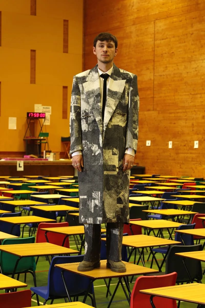 Model wearing bespoke tailored coat standing on desk in hall.