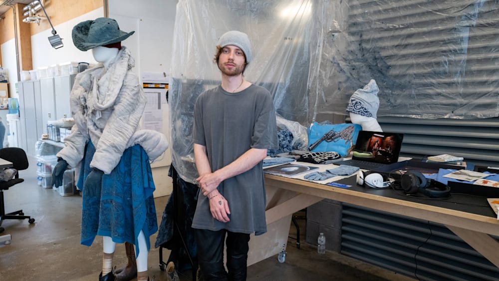 A student in a beanie hat standing next to a clothes rail with his denim collection.