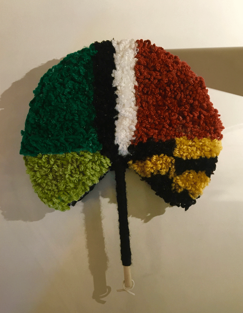 A traditional shaped hand fan made our of red, green, yellow, black and white fabric pattern