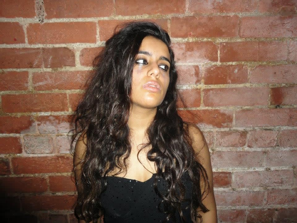 Vaidehi standing against an exposed brick wall. She has long dark hair, and she's looking off to the left