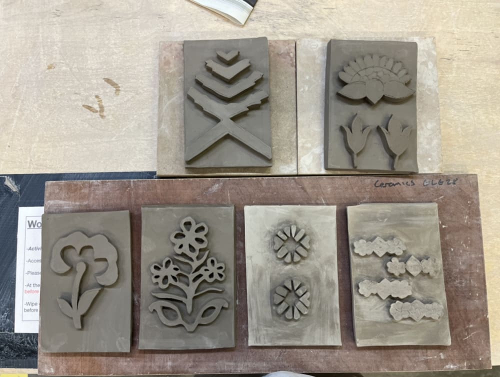 Six clay rectangle shaped pieces, each with an individual design on of a flower or plant.