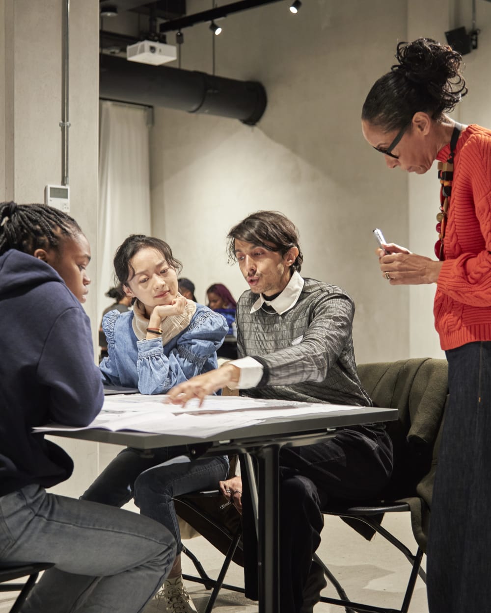 3 team members gather round a table discussing ideas while a coach listens. 