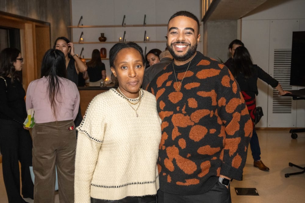 Two guests at the reception smiling at the camera. The lady on the left is wearing a cream jumper with navy stitch details around the seams; and the man on the left is wearing a large scale leopard print jumper.