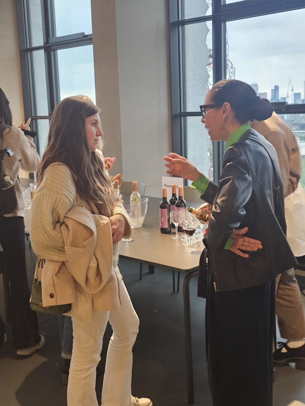 2 people standing infront of a table with drinks on it talking after an event. 