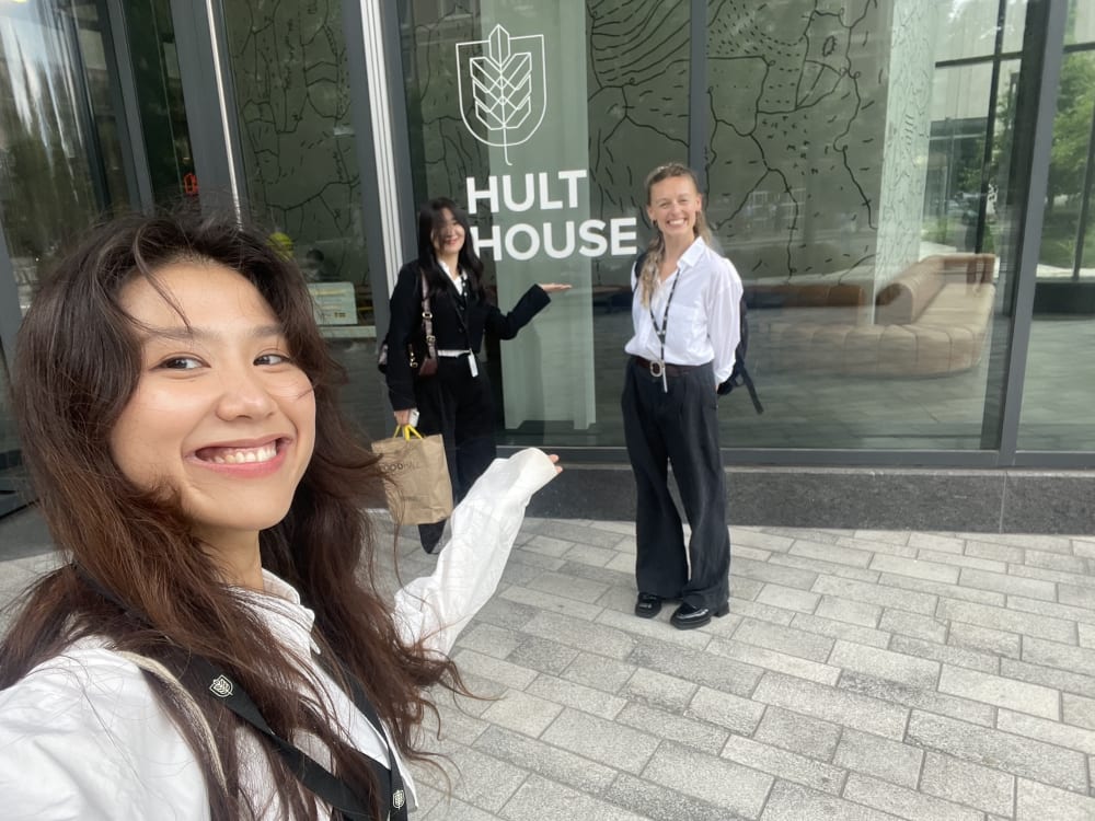 Three people outside large window with text 'Hult Prize' imprinted on.