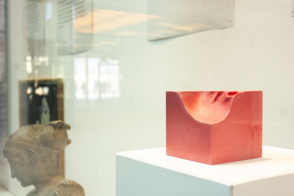 Red square sculpture placed on a table in an exhibition.