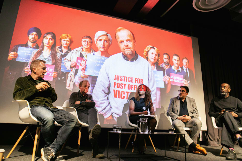 Panel guests on stage at a talk sit in front of a projection