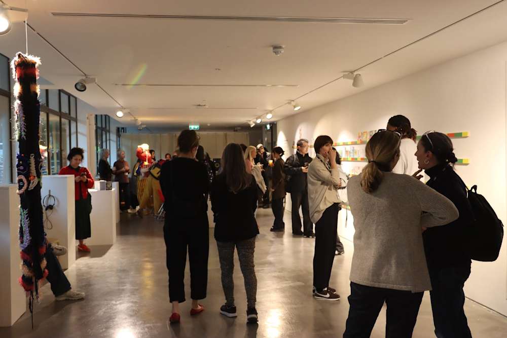 People gather in a modern gallery, engaging with vibrant wall art and sculptures. The atmosphere is lively and contemplative, fostering discussion.