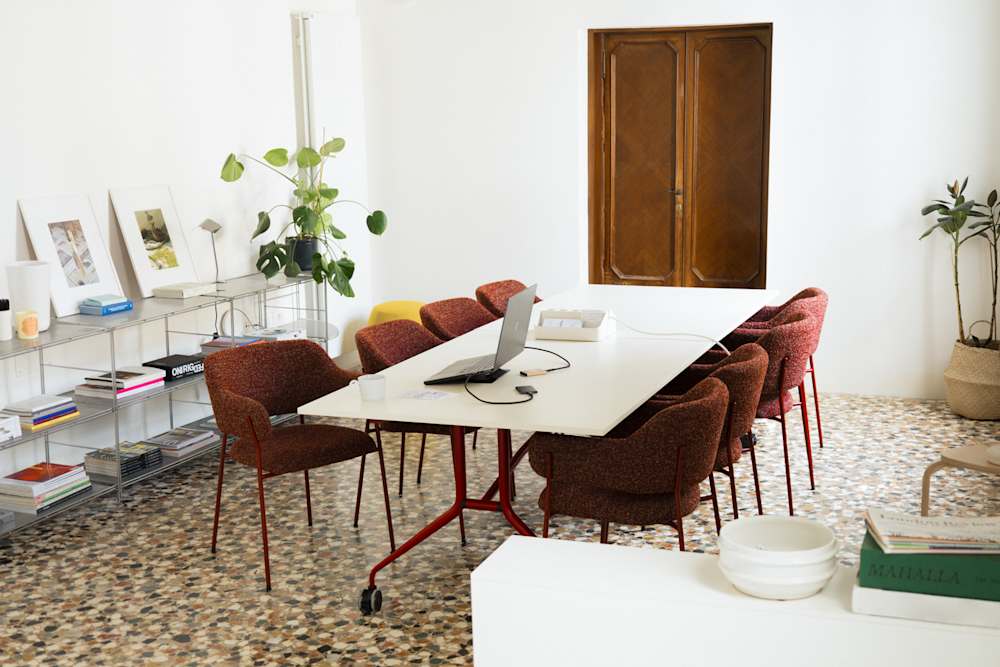Picture of a meeting room in Venice, showing a big table with red chairs at the center, and a steel bookshelf