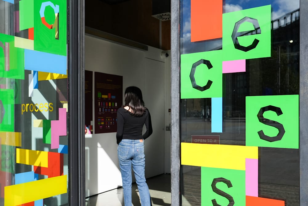 A person entering the process exhibition, surrounded on both sides by colourful block-based visuals and the typographic exhibition identity visuals