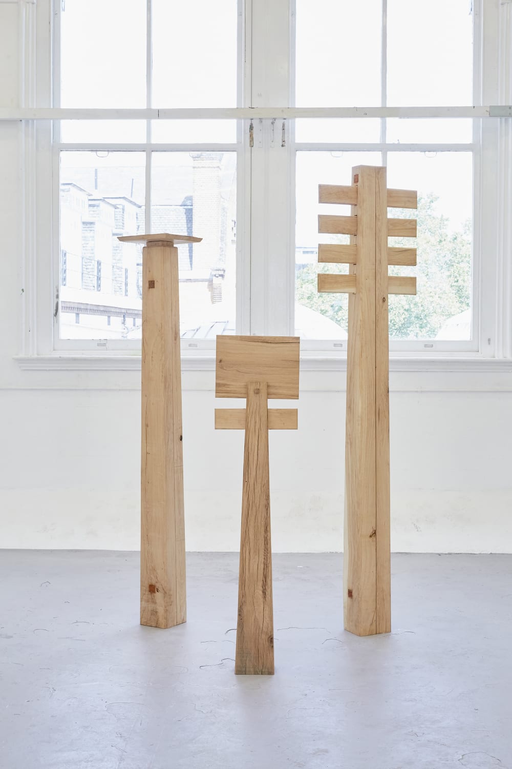 Three large wooden objects in front of a window in a bright, white room.