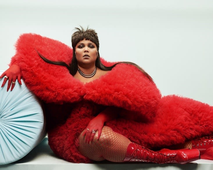 a portrait of Lizzo leaning on a cushion wearing a red dress