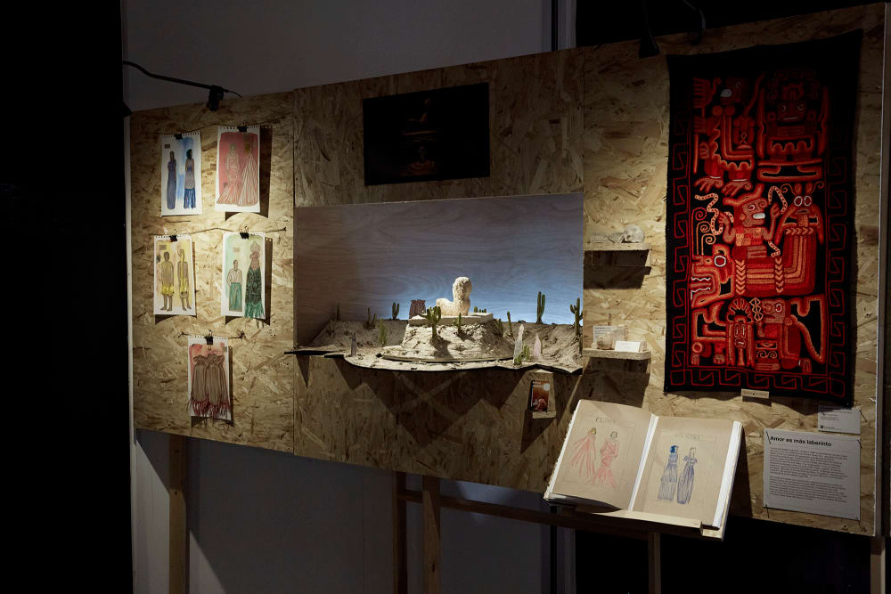 Image shows a woodchip board with artwork hanging on it. In the middle, there is an indent where a scale model for a set design can be seen.