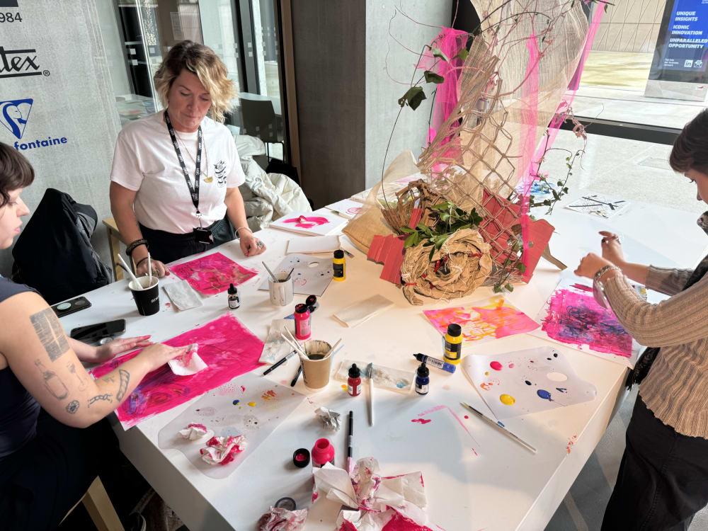 Three people standing at table using colourful paints. 