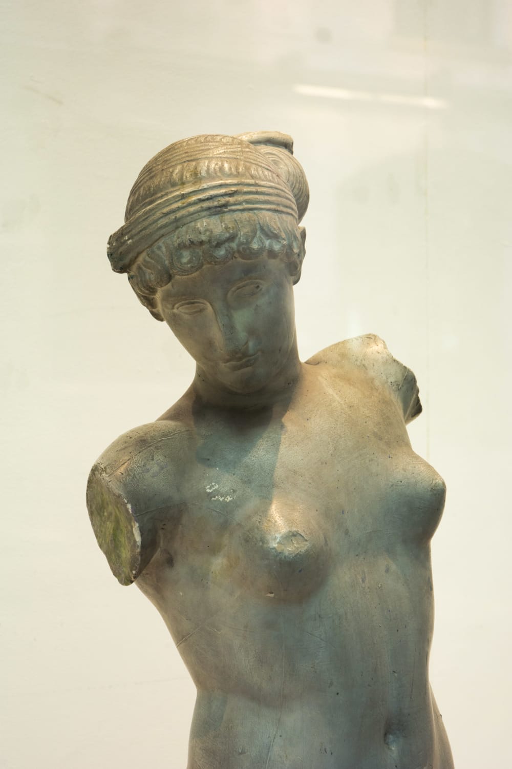 Grey sculpture of a female without arms with gaze and chin facing down.