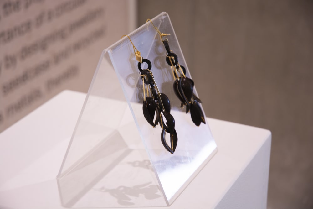 A pair of earring placed on a see-through glass holder behind a window in an exhibition. 