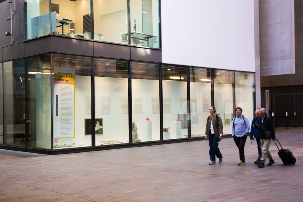 Three people walking past a lit-up window gallery display in the background.
