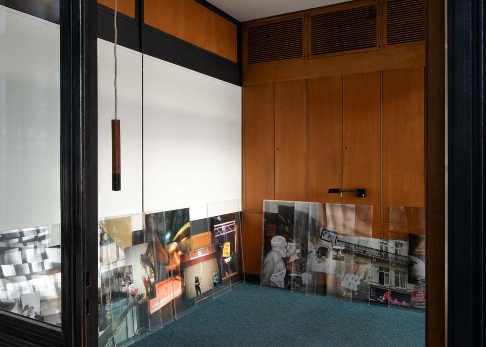 Layered photos resting on the floor, leaning against wood panelled walls