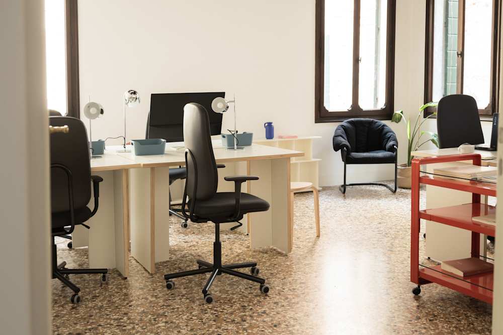 Picture of a working space including some wooden desks, laptops, and black chairs