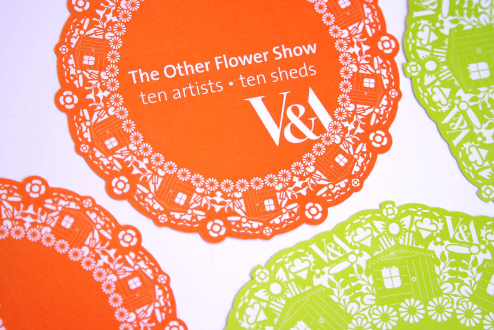 Two orange and two green doilies on a white background. The largest one is printed with text which reads The Other Flower Show, ten artists, ten sheds, V&A