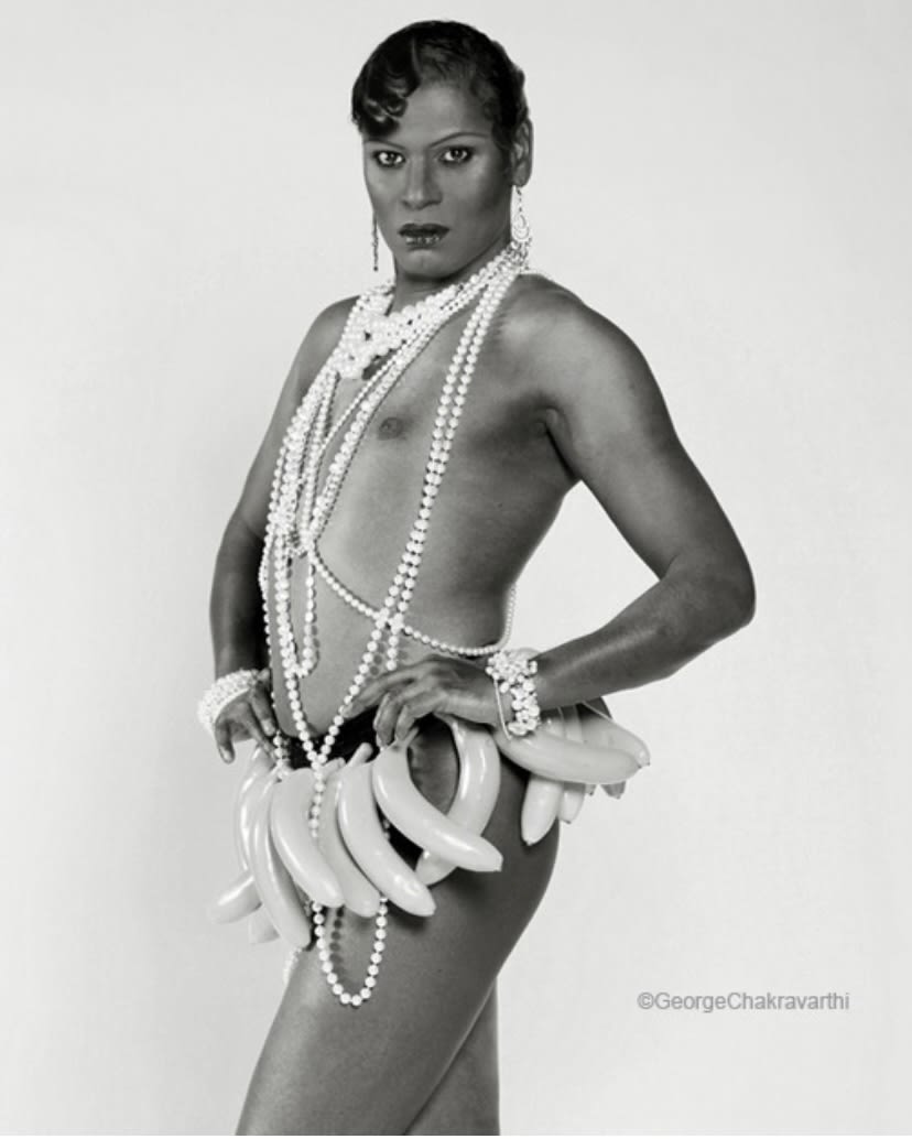 black and white portrait of person with bananas hanging from their belt wearing multiple pearl necklaces