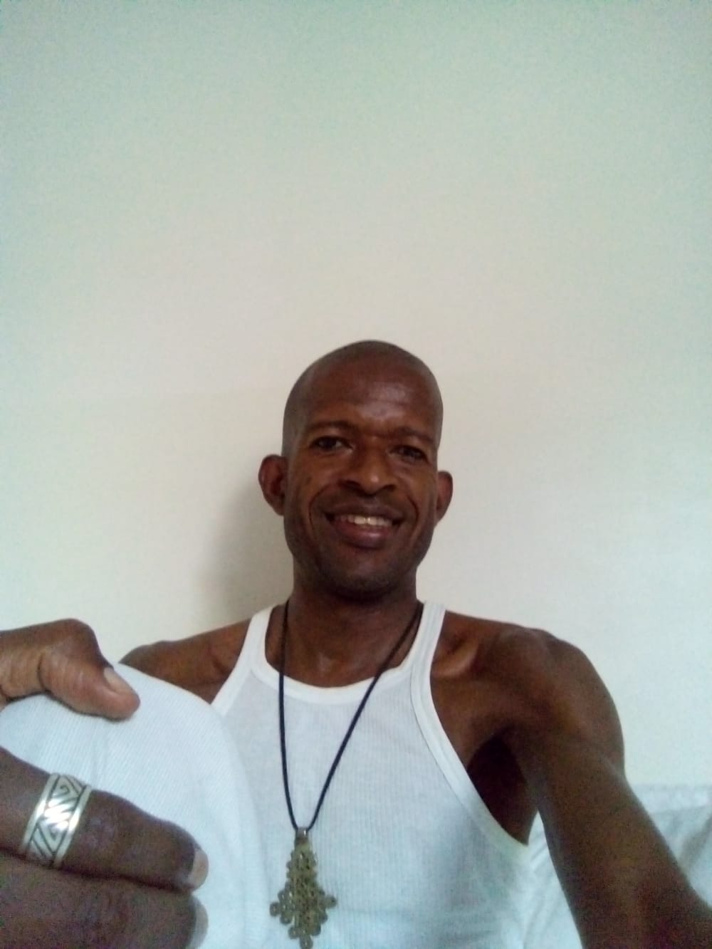 Photo of David - wearing a white vest and long chain necklace