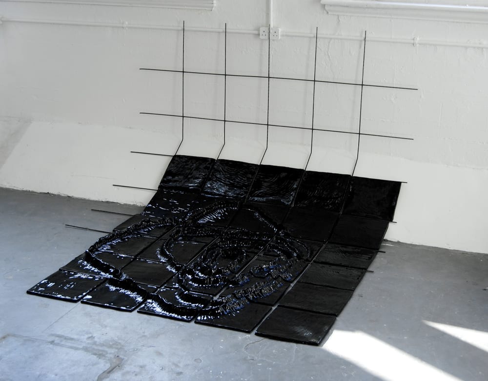 A black grid slumps against a wall, the lower portions of the grid are populated by black squares, a mountain range-like shape emerging upon them, each square containing a component of the piece which combine in the integration. 