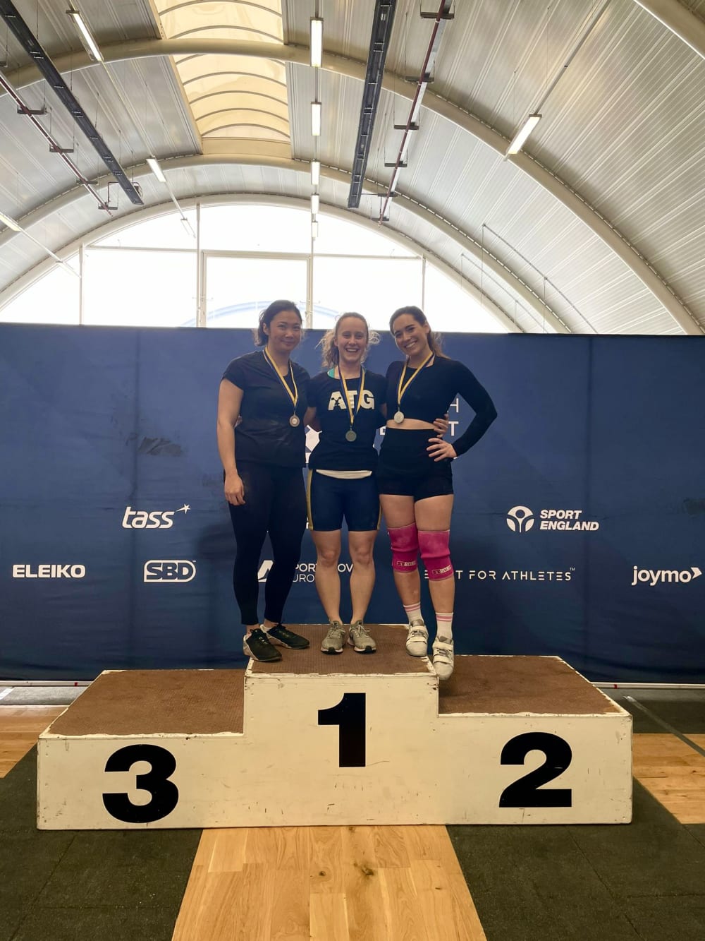 Three people posing for a picture on pedestals for their bronze, silver and gold medals.