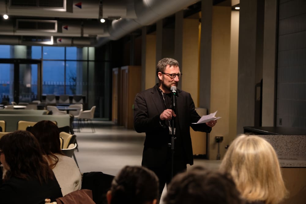 Person speaking in front of an audience with a mic at a gala dinner.