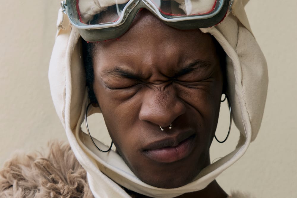 Model wearing goggles and headwear with eyes closed.