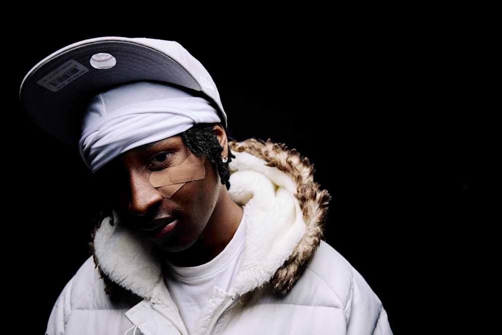 Slim, in white jacket and fur hood, with cap and plasters under one eye.