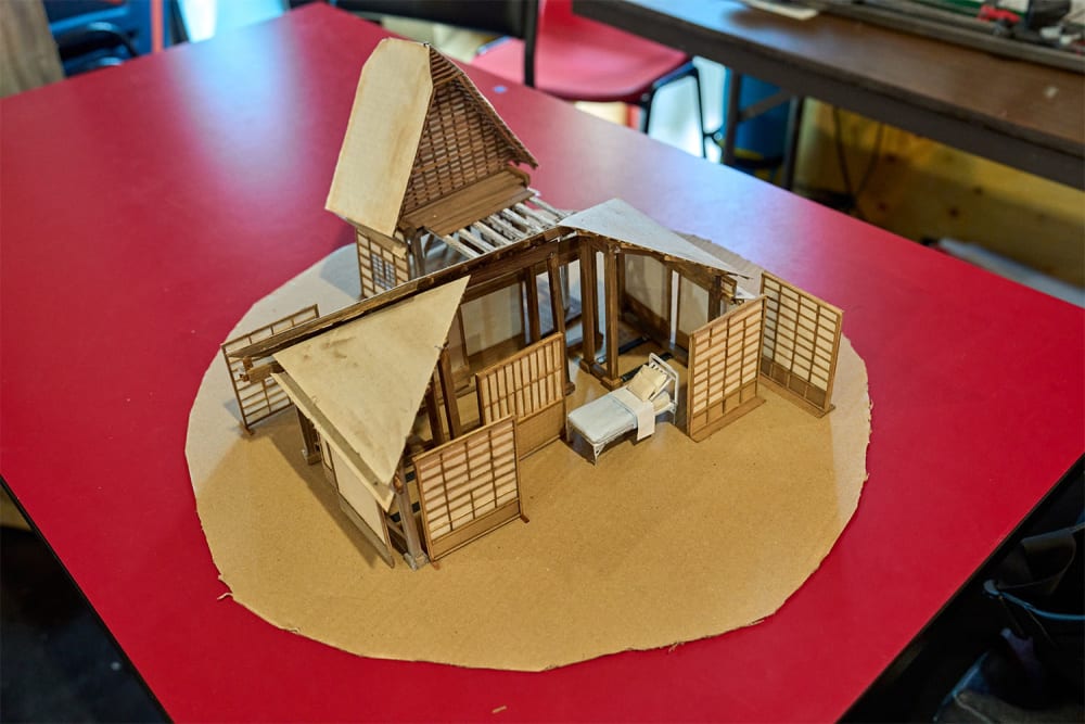 Image shows a miniature model of a wooden house sat on top of a red table