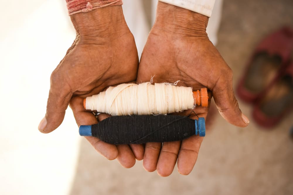 Two rolls of white and black thread being shown to the camera in cupped hands
