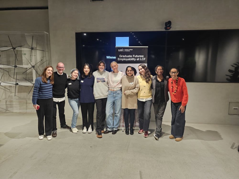 Winners and judges of of the LCF Hackathon standing in a row in a concrete room in front of a tv screen