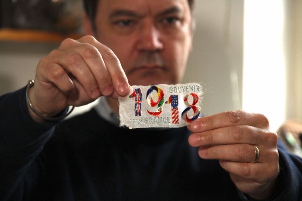 A man holding up a badge with '1918 souvenir' sewn onto it