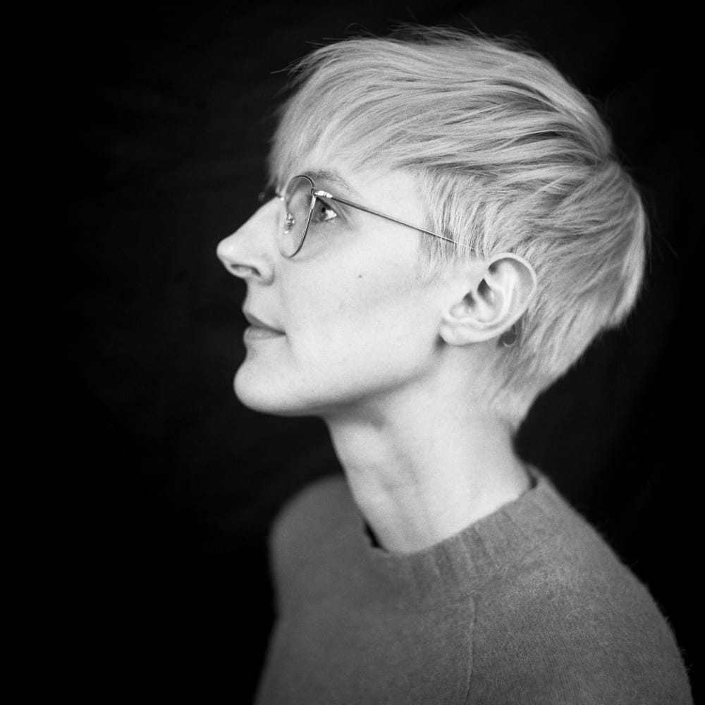 Black and white photo of Marie. She's in profile, with a cropped pixie cut and glasses