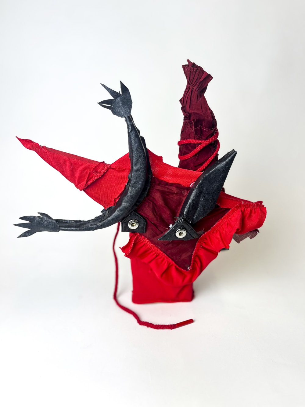 Red effigy sculpture made out of textile and wood against a white backdrop.